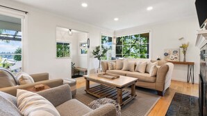 A modern living room with a sofa, coffee table, and a view of greenery outside. - Sunset Garden Retreat-Sea & Mountain View w/ Sauna (Bremerton)