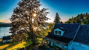 A house with a large tree in front, a garage, and a view of a body of water. - Sunset Garden Retreat-Sea & Mountain View w/ Sauna (Bremerton)