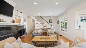 A spacious living room with a fireplace, a staircase, and a large window providing a view of the outdoors. - Sunset Garden Retreat-Sea & Mountain View w/ Sauna (Bremerton)