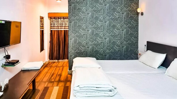 Quarto de hotel com cama, televisão, ar condicionado fixado na parede e papel de parede estampado.