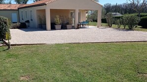 Une maison dotée d’un patio couvert, d’une allée en gravier et d’une pelouse.