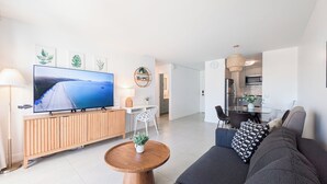A modern living room with a flat-screen TV, wooden furniture, a dining area, and a kitchen. - High Floor 2BR/2BA+Den 5beds Partial Ocean View + 1 Parking 1 min from the beach (Honolulu)