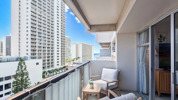 A balcony with a view of tall buildings, a small table with a plant, and a chair. - High Floor 2BR/2BA+Den 5beds Partial Ocean View + 1 Parking 1 min from the beach (Honolulu)