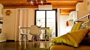 Een moderne keuken met witte kastjes, een eethoek met witte stoelen, en een gezellige woonkamer met een groen vloerkleed en een bank.