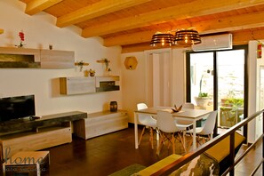 Una cocina moderna con zona de comedor, vigas de madera en el techo y un ventanal con plantas en macetas.