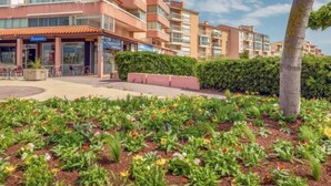 Een meerlaags woongebouw met balkons, een restaurant en een aangelegde tuin met diverse planten en bloemen.
