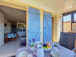 A dining area with a table set for four, a kitchen in the background, and a balcony with a railing.