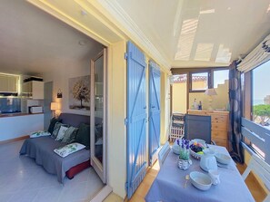 A compact living space with a kitchenette, a dining area with a table set for two, and a balcony with a view.