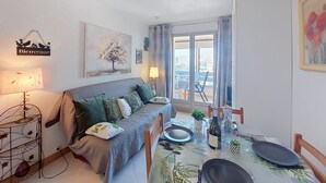 Una sala de estar acogedora con un sofá, una mesa de comedor para dos personas, un balcón con vistas y un cartel que dice 'Bienvenue'.