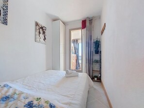 Une chambre à coucher avec un lit, une armoire, une plante en pot et une porte donnant sur une autre pièce.