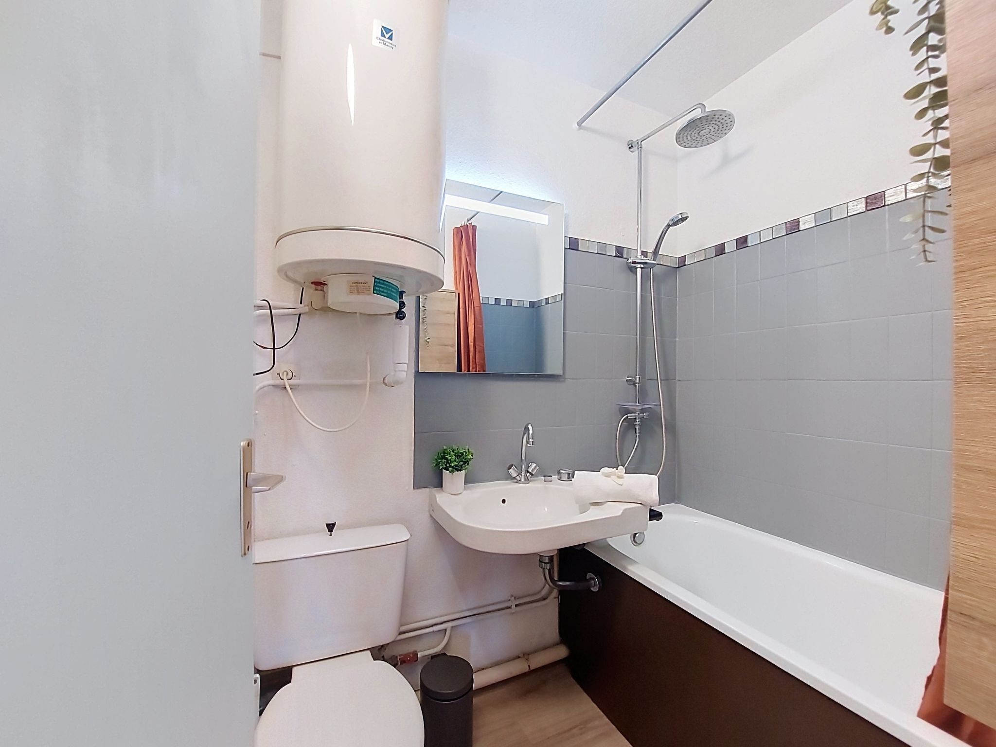 Un baño con inodoro, lavabo, ducha y una pequeña planta en maceta.