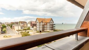Un balcon offrant une vue sur une ville côtière, avec un mélange de bâtiments résidentiels et d’une plage.