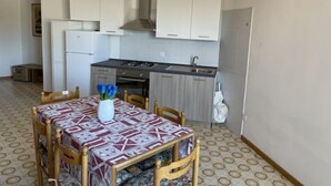A compact kitchen with white cabinets, a gas stove, and a sink. There's a dining table with a patterned tablecloth and a vase of blue flowers. - Canaima by Interhome (Bibione)