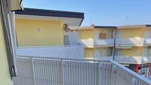 A balcony with a red-tiled floor, white metal railing, and a yellow building in the background. - Canaima by Interhome (Bibione)