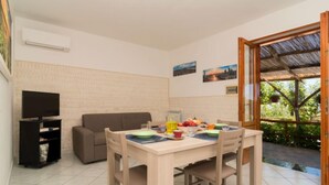 Zona pranzo con tavolo apparecchiato per due, divano, televisore e cestino.