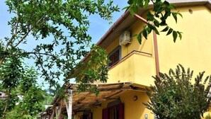 Un edificio giallo con una pergola in legno, mobili da esterno e diverse piante.
