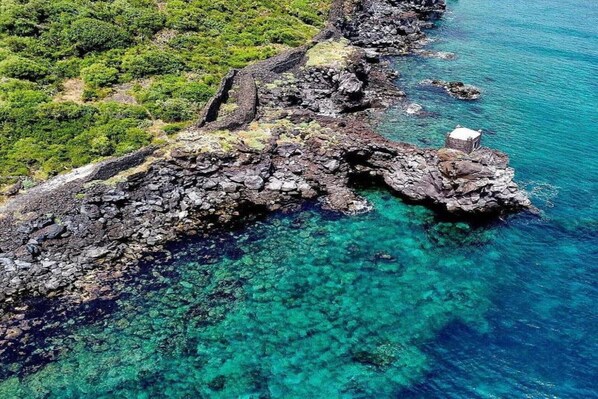 Une côte rocheuse bordée d’une eau turquoise cristalline et sur laquelle se trouve un petit bâtiment.