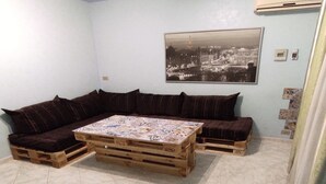 A room with a wooden pallet sofa, a table with a patterned tablecloth, and a cityscape photograph on the wall.