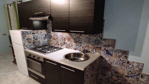 A compact kitchen with dark cabinets, a gas stove, a sink, and decorative tiles.