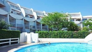 En swimmingpool med en person i vandet, omgivet af en moderne bygning med altaner og en klar himmel.