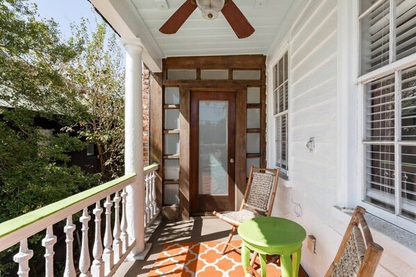 A covered porch with a wooden door, a green table, and a chair.