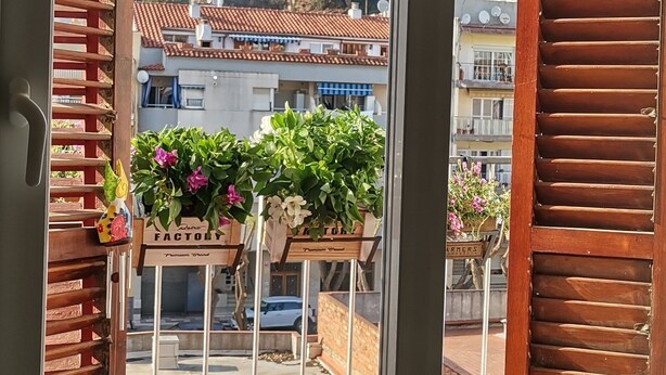 Ein Balkon mit Holzklappläden, Blumentöpfen und Blick auf Gebäude im Hintergrund.