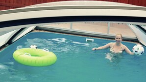 Une piscine avec une personne dans l’eau, un flotteur gonflable vert en forme de cercle et un ballon.