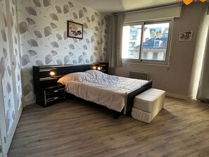 A bedroom with a bed, bedside tables, a window, and a view of buildings outside.