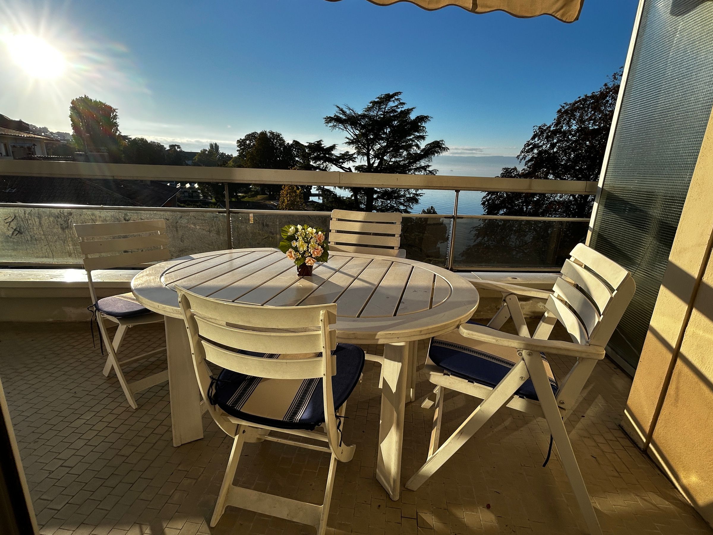 A round table with chairs on an outdoor patio with a view of the sea.