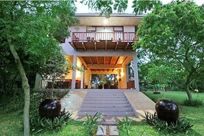 Stunning two-story building with a balcony and covered porch, surrounded by lush greenery and beautiful vases.