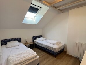 Un petit logement composé d’une seule pièce, avec deux lits, une lucarne et un radiateur.