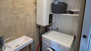 A compact bathroom with a washing machine, a sink, and a shelf with a basket. - Charming house for 4 near town center (Sarzeau)