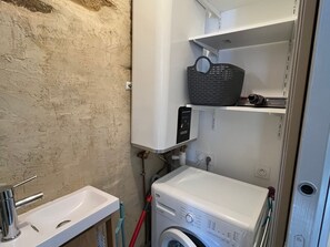 Un bagno compatto con lavatrice, lavabo e ripiano contenente un cesto.