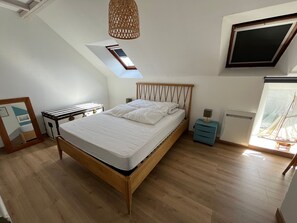 A bedroom with a bed, a desk, a small table, a nightstand, a wall-mounted TV, and a window with a view.