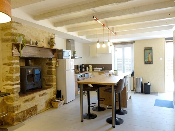Una cocina con pared de piedra, estufa de leña, electrodomésticos modernos y un comedor con taburetes de bar.