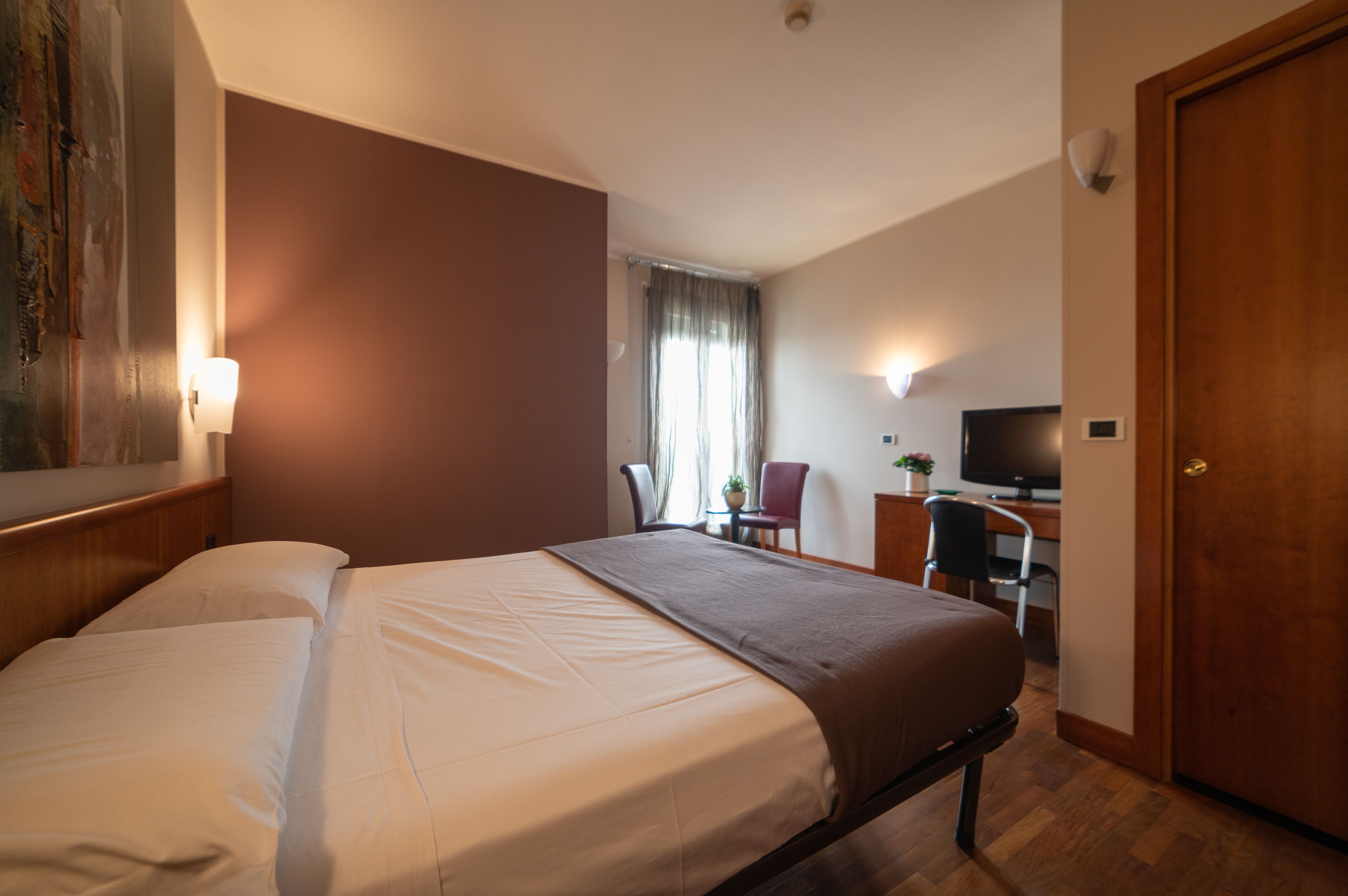 Une chambre d’hôtel avec un lit, un bureau, une chaise, une télévision et une porte.