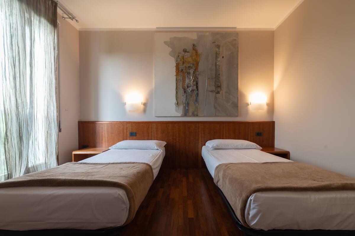 Ein Hotelzimmer mit zwei Einzelbetten, Holz-Kopfteilen, einem großen abstrakten Gemälde an der Wand und zwei Wandleuchten.