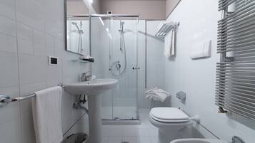 Un baño moderno con ducha envuelta en vidrio, lavamanos pedestal, inodoro y bidé.