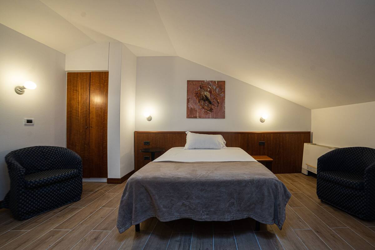 Ein Schlafzimmer mit einem Bett, zwei Stühlen, einer Holztür und einem Bild an der Wand.