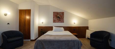 A bedroom with a bed, two chairs, a wooden door, and a painting on the wall.