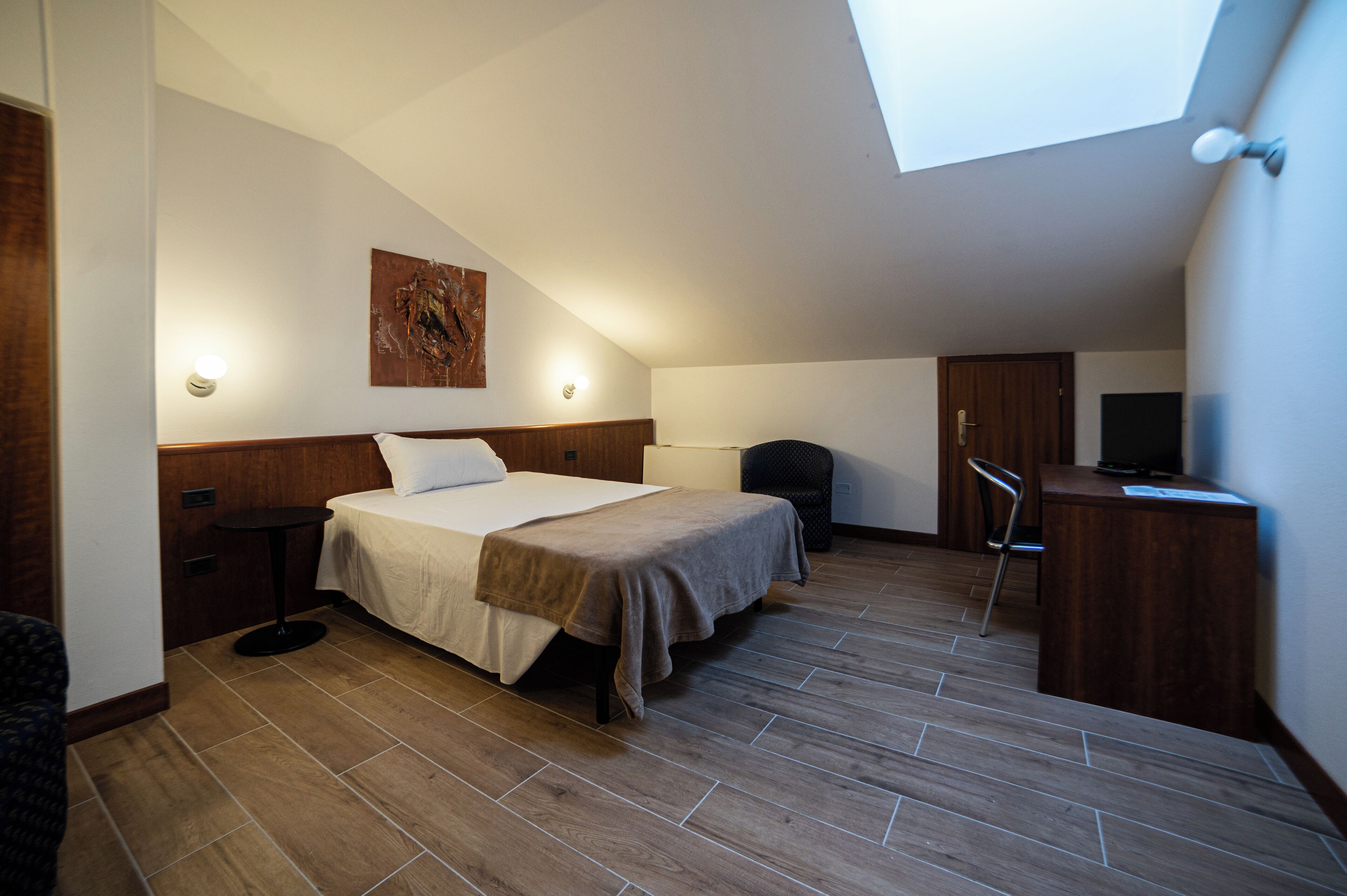 A small, modern bedroom with a skylight, a bed, a desk, and a chair.