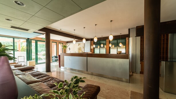 Een moderne lobby met een receptiebalie, een zithoek en grote ramen.