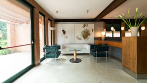 Een moderne lobby met een glazen scheidingswand, een receptiebalie en een zithoek met twee stoelen en een ronde tafel.
