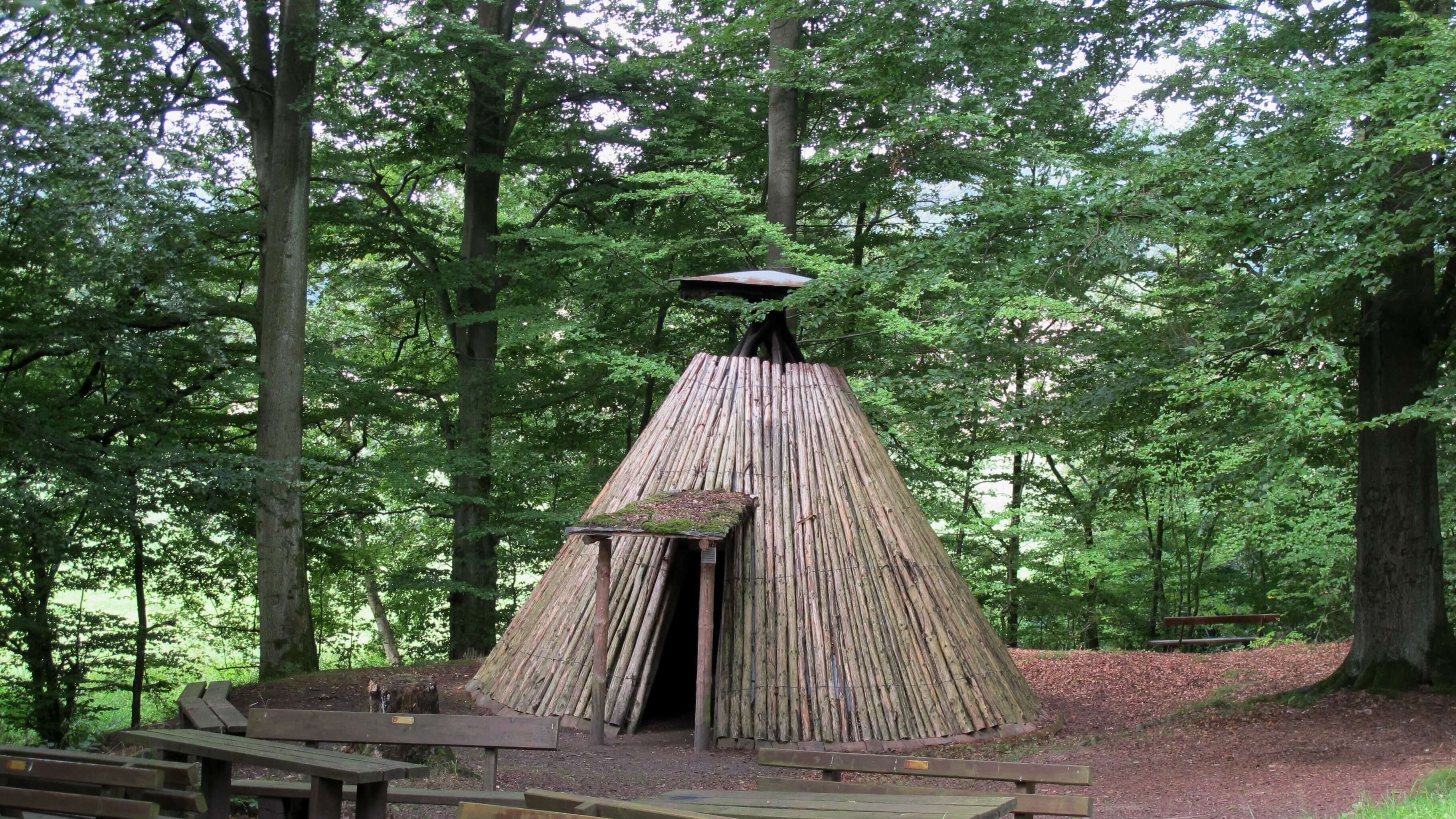 Eine rustikale Holzhütte mit einem Strohdach, umgeben von einem Wald.