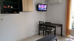 Una pequeña sala de estar con televisor, un mueble de madera, una mesa de comedor con sillas y un banco.