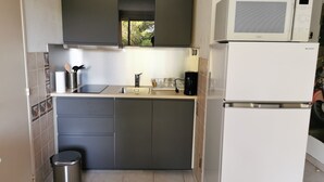 Una cocina compacta con armarios oscuros, un lavamanos de acero inoxidable, un microondas y una cafetera.