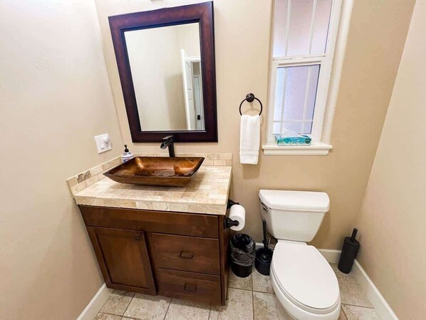 A bathroom with a wooden vanity, a large mirror, a white toilet, and a window with a towel rack. - Peaceful Spot | Private Backyard | King Bed | AC! (Columbia Falls)