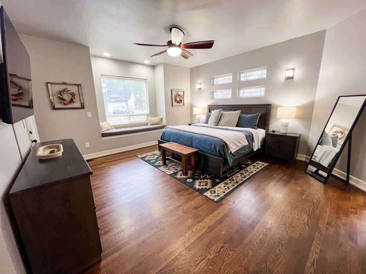 Une chambre à coucher comprenant un lit, des tables de chevet, un ventilateur de plafond, une fenêtre et un petit tapis.