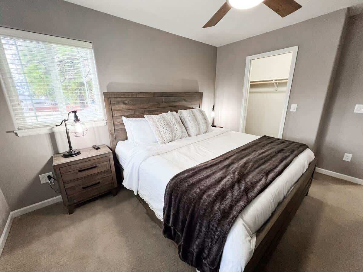 Een slaapkamer met een bed, nachtkastje, lamp en een plafondventilator.