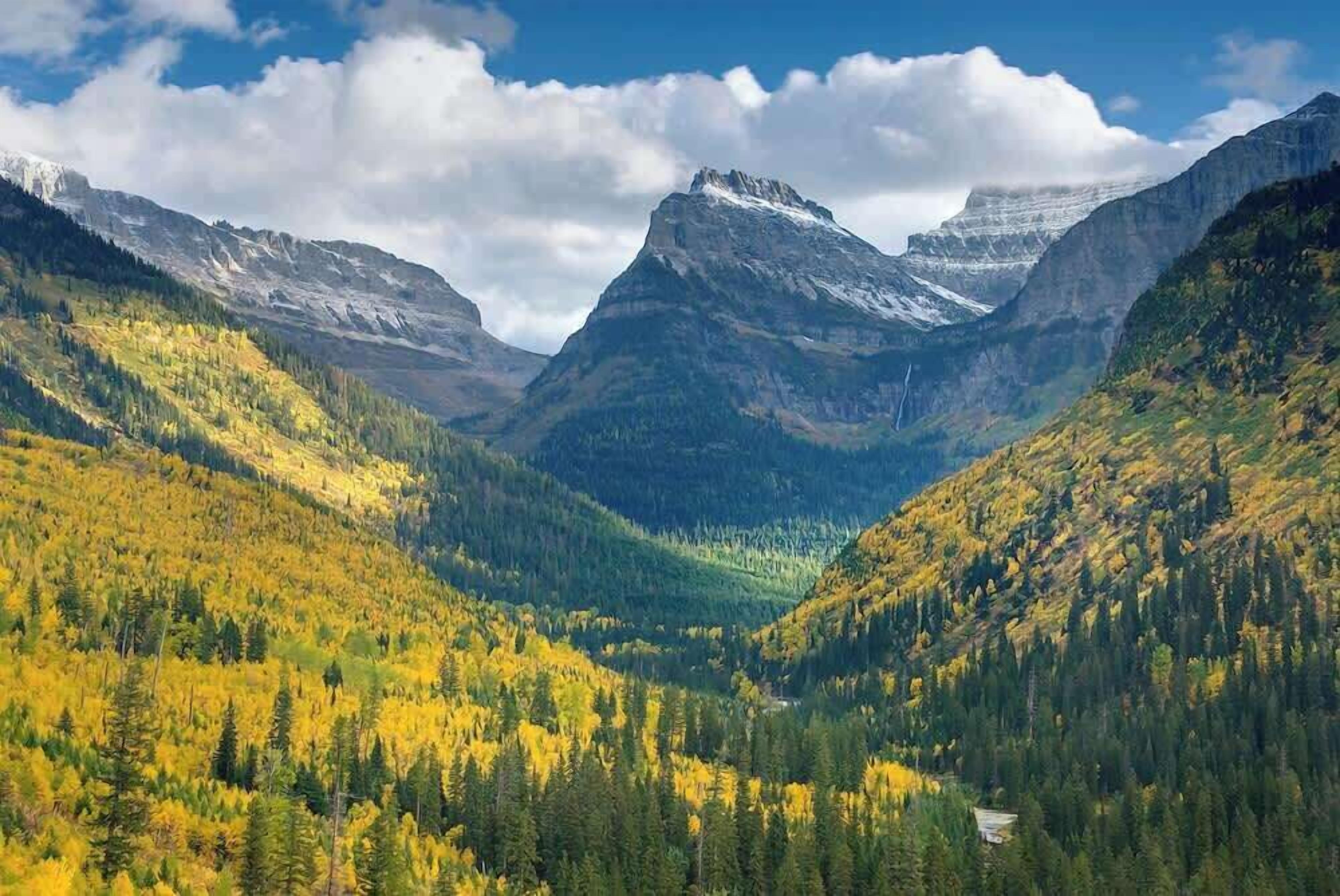Un paisaje montañoso con un valle y una casa ubicada entre los árboles.